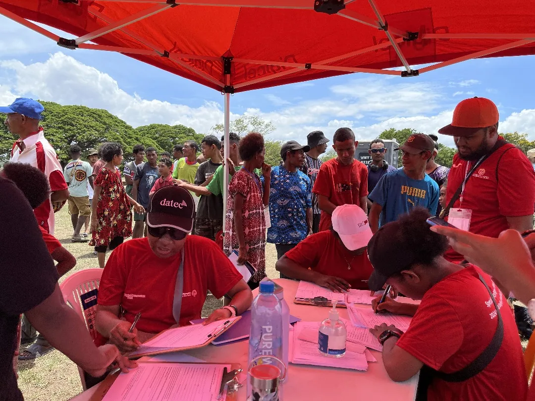 Community members gather beneath a red event shelter